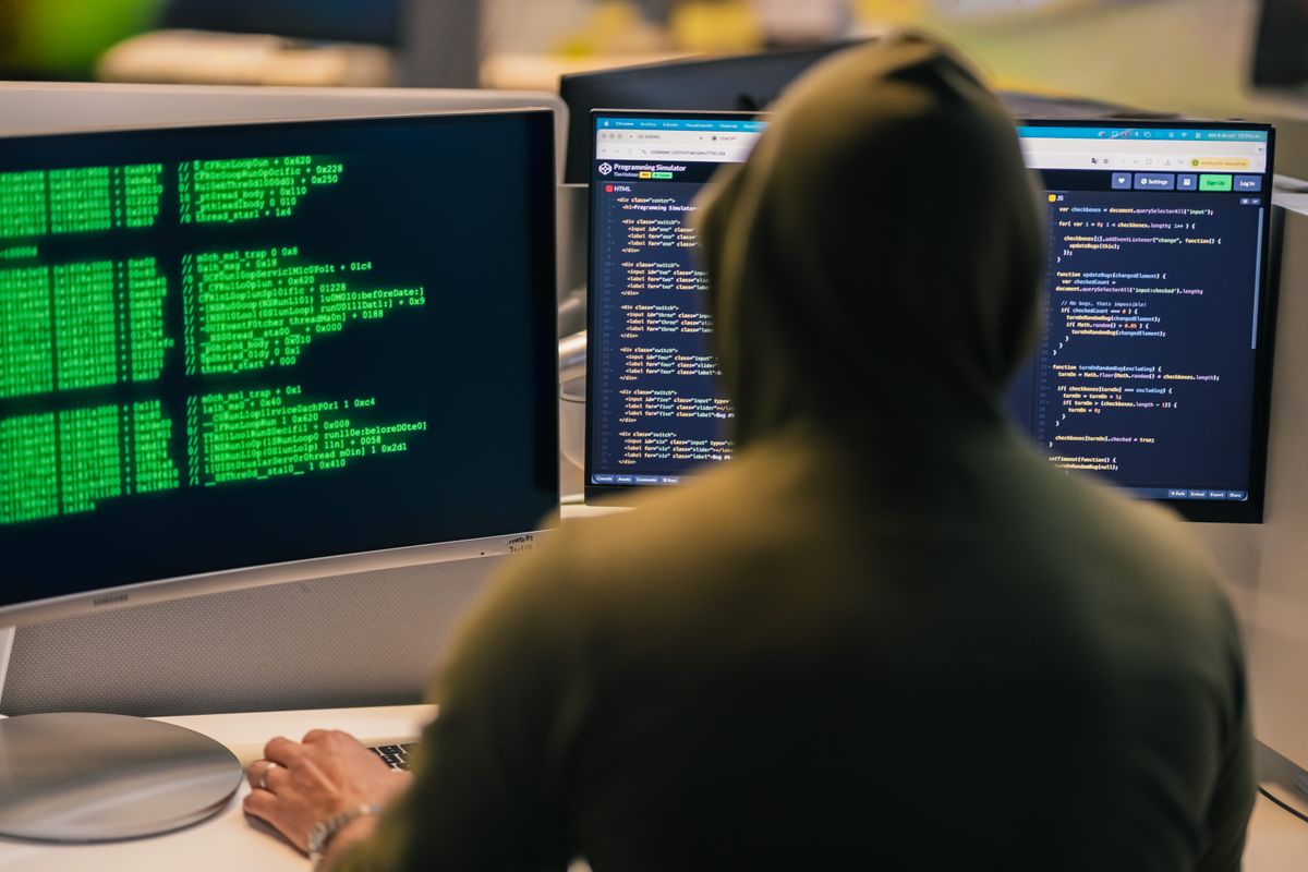A developer coding on multiple monitors in a dark room for a data scraping project